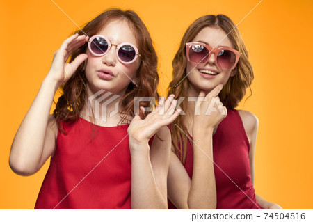 Happy sisters in red dresses on a yellow background are having fun and gesticulating Copy Space Happy sisters in red dresses on a yellow background are having fun and gesticulating Copy Space 74504816