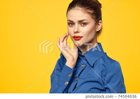 Portrait of a woman in a blue shirt with bright makeup red lips yellow background cropped view 74504836