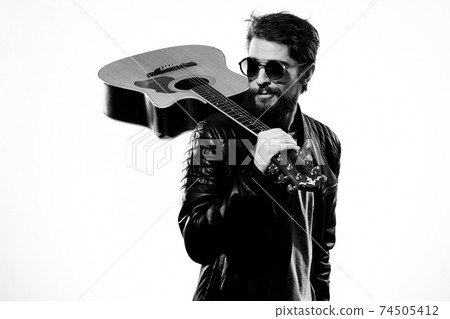 A man holds a guitar in his hands black leather jacket dark glasses music performance light background 74505412