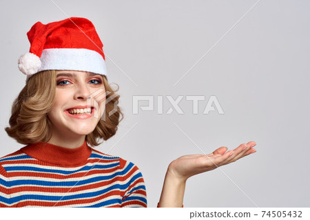 Happy woman in a Christmas cap and a striped sweater gestures with her hands for the New Year holidays 74505432