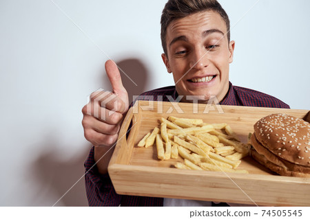 Man eating wooden pallet fast food french fries hamburger diet food restaurant light background Man eating wooden pallet fast food french fries hamburger diet food restaurant light background 74505545