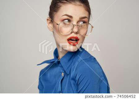 Portrait of emotional woman in blue shirt and glasses bright makeup model light background cropped view Copy Space 74506452