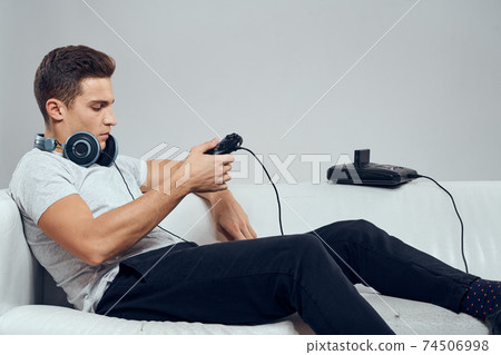 A man lies on the couch headphones gamepad consoles technology entertainment video games A man lies on the couch headphones gamepad consoles technology entertainment video games 74506998