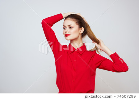 A beautiful girl with red lips and a shirt on a light background gestures with her hands A beautiful girl with red lips and a shirt on a light background gestures with her hands 74507299