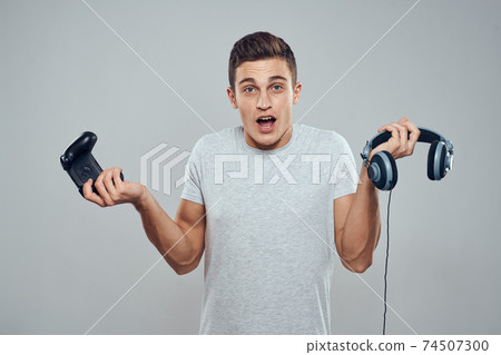 Man with headphones and joystick in hands technology entertainment video games lifestyle addiction light background Man with headphones and joystick in hands technology entertainment video games lifestyle addiction light background 74507300
