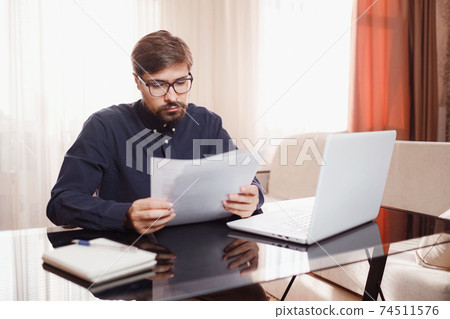 Entrepreneur works with a laptop and keeps a document in a home office 74511576