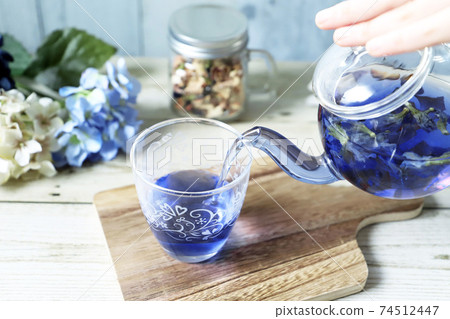 Pour butterfly pea blue herbal tea from a glass teapot into a cup 74512447