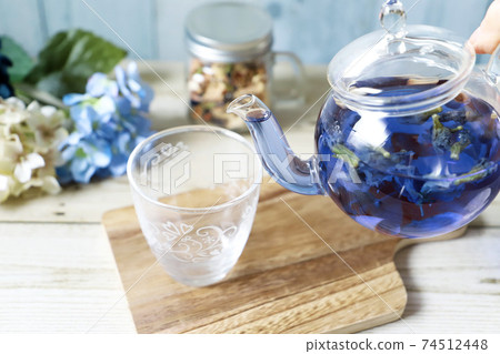 Pour butterfly pea blue herbal tea from a glass teapot into a cup 74512448