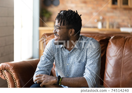 Close up dreamy smiling African American man sitting on couch 74514240