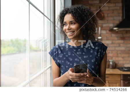Close up dreamy smiling African American woman holding smartphone Close up dreamy smiling African American woman holding smartphone 74514266
