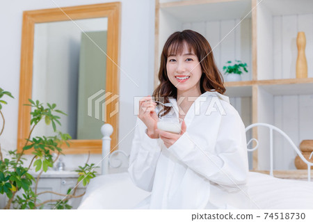 Young woman eating yogurt in bed Young woman eating yogurt in bed 74518730