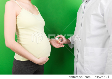 Male gynecologist giving pills to pregnant woman during appointment at colored background. Visit To A Doctor Pregnancy Healthcare And People Concept 74524321