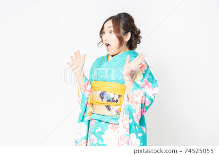 A woman in furisode standing in front of a white background and making a surprised pose 74525055