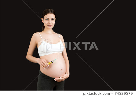 pregnant woman holding a syringe against her belly at colorful background with copy space. Injection during pregnancy concept pregnant woman holding a syringe against her belly at colorful background with copy space. Injection during pregnancy concept 74529579