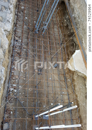 Reinforcement of a concrete basis. The location of the foundation of the new building, parts and fittings made of steel rods and wire, which are being prepared for pouring cement, construction works. Reinforcement of a concrete basis. The location of the foundation of the new building, parts and fittings made of steel rods and wire, which are being prepared for pouring cement, construction works. 74529964