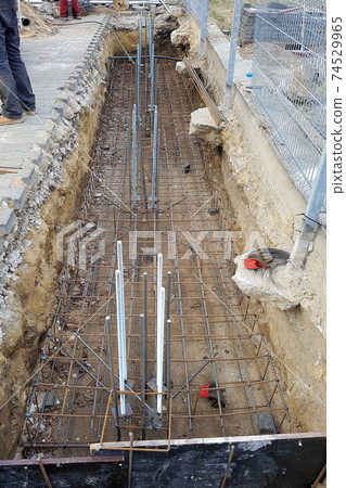 Reinforcement of a concrete basis. The location of the foundation of the new building, parts and fittings made of steel rods and wire, which are being prepared for pouring cement, construction works. 74529965