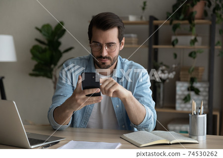 Serious young guy student check uncertain information online using smartphone Serious young guy student check uncertain information online using smartphone 74530262
