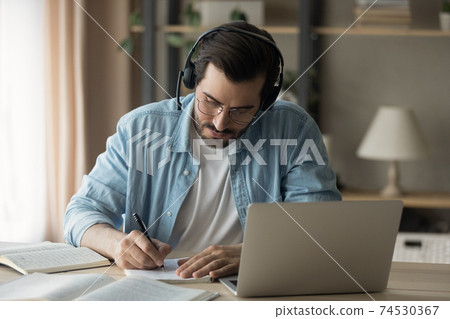 Millennial man focused on remote work make translation using laptop Millennial man focused on remote work make translation using laptop 74530367
