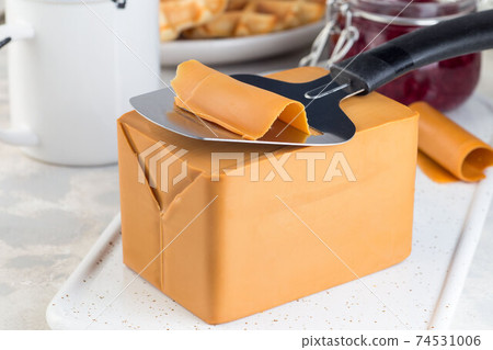 Piece of Norwegian brown cheese with cheese slicer, horizontal, closeup 74531006