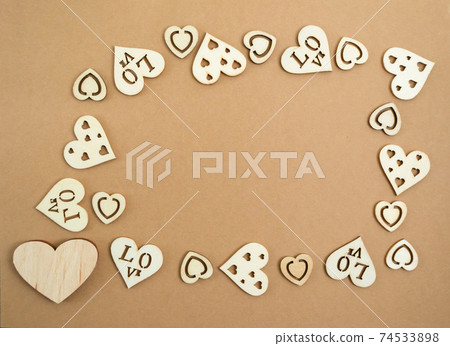 Wooden hearts on a pastel craft paper background in the form of a frame. Abstract background with wood cut shapes. Sainte Valentine. Copy space. 74533898