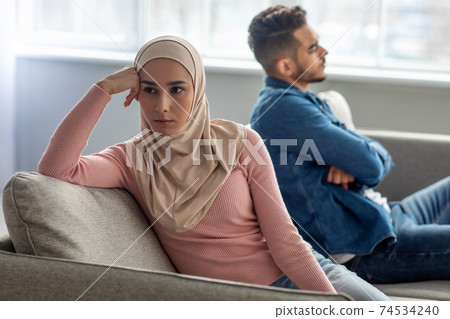 Upset woman in hijab sitting by her sad husband 74534240