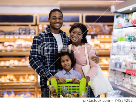 Portrait of smiling black parents with their daughter purchasing groceries at big supermarket Portrait of smiling black parents with their daughter purchasing groceries at big supermarket 74534292