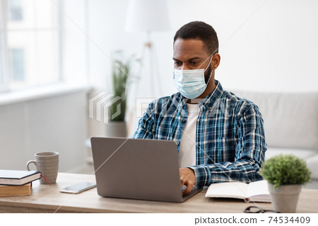 African Man At Laptop Wearing Protective Face Mask Working Indoors African Man At Laptop Wearing Protective Face Mask Working Indoors 74534409