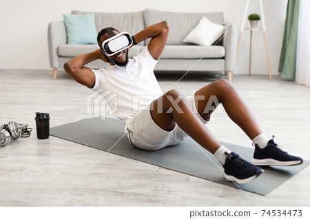 African Man Wearing VR Glasses Doing Abs Exercise At Home African Man Wearing VR Glasses Doing Abs Exercise At Home 74534473
