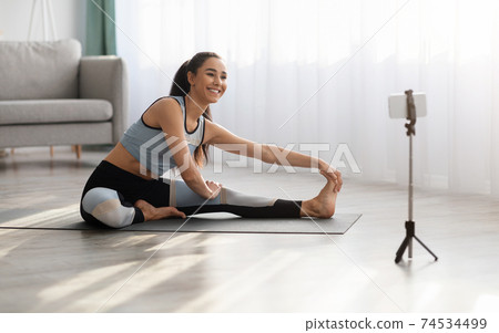 Cheerful sporty woman stretching on fitness mat, using smartphone Cheerful sporty woman stretching on fitness mat, using smartphone 74534499