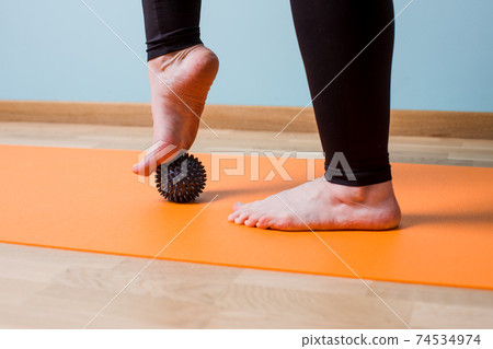 Massaging bare feet with small knobbed ball 74534974