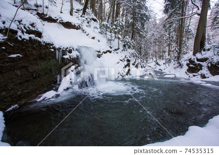 the stream flows in a snowy forest 74535315