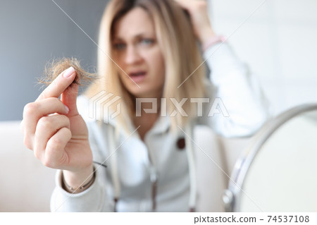 Frustrated woman holds bun of her hair in her hand 74537108