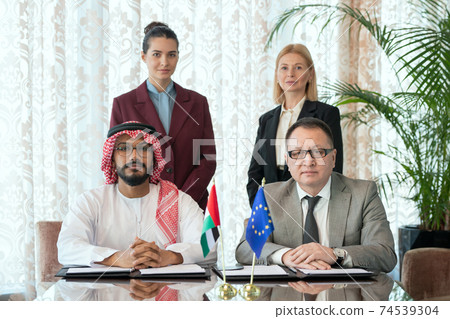 Two successful business partners or delegates in formalwear sitting by table 74539304