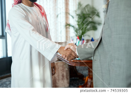 Successful Arabian businessman in national attire greeting his foreign partner Successful Arabian businessman in national attire greeting his foreign partner 74539305