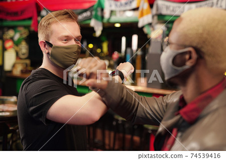 Two intercultural guys in protective masks giving one another elbow bump 74539416