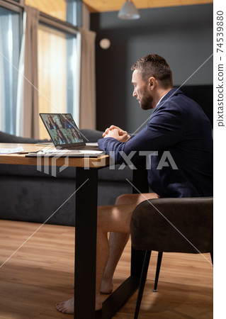 Young businessman in dark blue jacket and underpants sitting in front of laptop 74539880