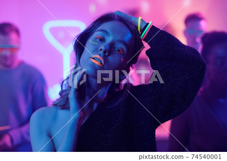 Young woman with glamorous neon makeup standing against her friends at party Young woman with glamorous neon makeup standing against her friends at party 74540001