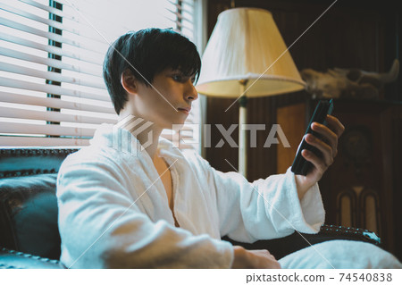 A man in a bathrobe looking at a smartphone 74540838