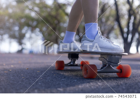 Close-up Asian women surf skate or skateboard outdoors on beautiful morning. Happy young women play surf skate at park on morning time. Close up Asian women leg wear sneaker paly surf skate on public 74543071