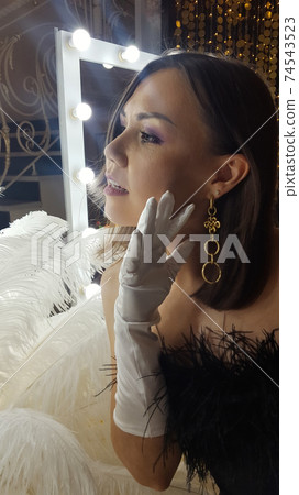 Beautiful asian young woman and decorative ostrich feathers on a gold table next to a make-up mirror. Get ready for the getsby party Beautiful asian young woman and decorative ostrich feathers on a gold table next to a make-up mirror. Get ready for the getsby party 74543523