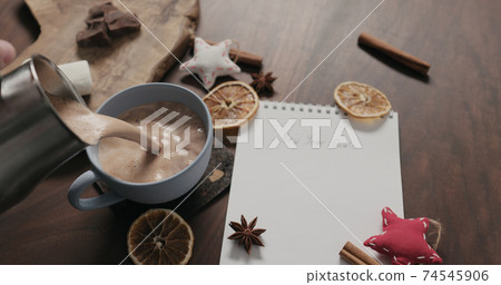 pour hot chocolate into blue cup with new year goals list in notepad 74545906