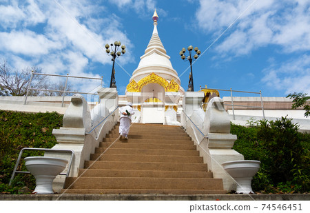 Chiang Rai Province,Chiang Saen,THAILAND-FEBRUARY 9,2021:A nun is walking up the fire stairs at the white pagoda. The Putta Nimit Chedi at Wat Phra Borommathat and blue sky with clouds. 74546451