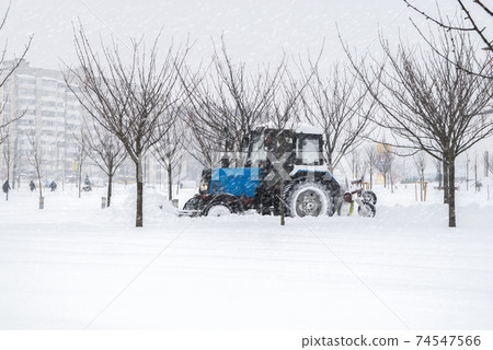 Snow-covered street. Snowplow removing snow from city road. Heavy snowstorm, blizzard traffic. Climate weather disaster. Winter urban scene. Snowdrifts after a snowfall Snow-covered street. Snowplow removing snow from city road. Heavy snowstorm, blizzard traffic. Climate weather disaster. Winter urban scene. Snowdrifts after a snowfall 74547566