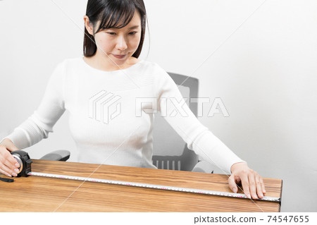 A sitting woman measuring with a tape measure A sitting woman measuring with a tape measure 74547655