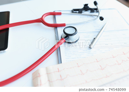Stethoscope and electrocardiogram lying on patients medical history closeup Stethoscope and electrocardiogram lying on patients medical history closeup 74548099