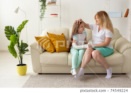Child with broken arm and gypsum spend time at home with mother. Childhood illnesses, a positive outlook and recovery. 74549224