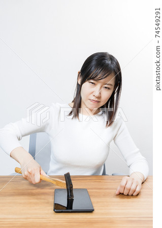 A woman trying to break a tablet with a hammer 74549291