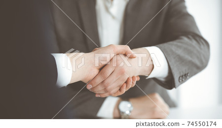 Unknown businessman shaking hands with his colleague or partner above the glass desk in modern office, close-up. Business people group at meeting 74550174