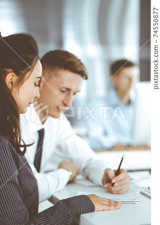 Business woman and man are discussing questions while using computer and blocknote in modern office, close-up. Teamwork in business Business woman and man are discussing questions while using computer and blocknote in modern office, close-up. Teamwork in business 74550877