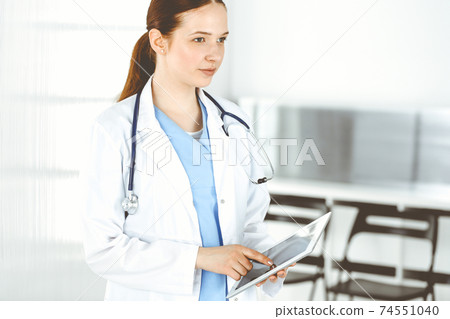 Woman-doctor or intern student at work. Female physician using tablet computer while standing in clinic. Medicine and health care concept Woman-doctor or intern student at work. Female physician using tablet computer while standing in clinic. Medicine and health care concept 74551040